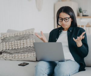 woman sitting on couch with laptop on lap looking frustrated